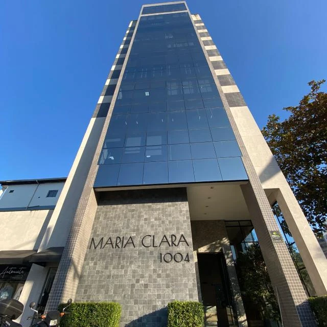 Fachada do Edifício Maria Clara, número 1004, vista de baixo para cima contra o céu azul; a torre de vidro escuro afina em direção ao topo.